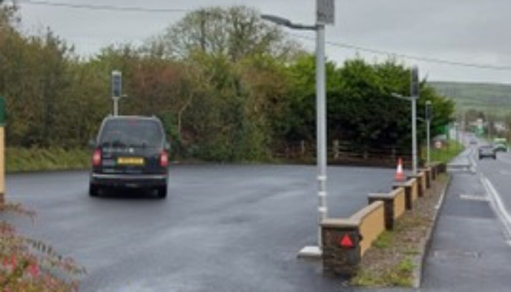 DBS805 lighting car park, A dark van is parked on a wet asphalt surface near a row of solar-powered streetlights and a low stone wall bordering a road.